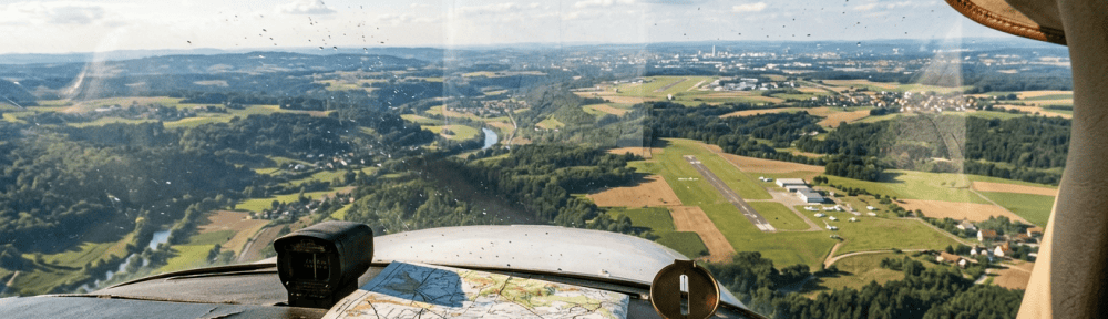 Cockpit view over farmland, river, villages, and a runway with map and compass